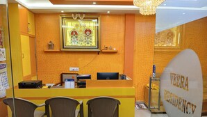 A reception desk with a computer, a calendar, and a sign reading "VEERA RESIDENCY". There are three wicker chairs in front of the desk. - Veera Residency (Gingee)