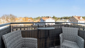 Een balkon met rieten meubilair en een tafeltje, met uitzicht op een woonwijk met huizen en bomen.