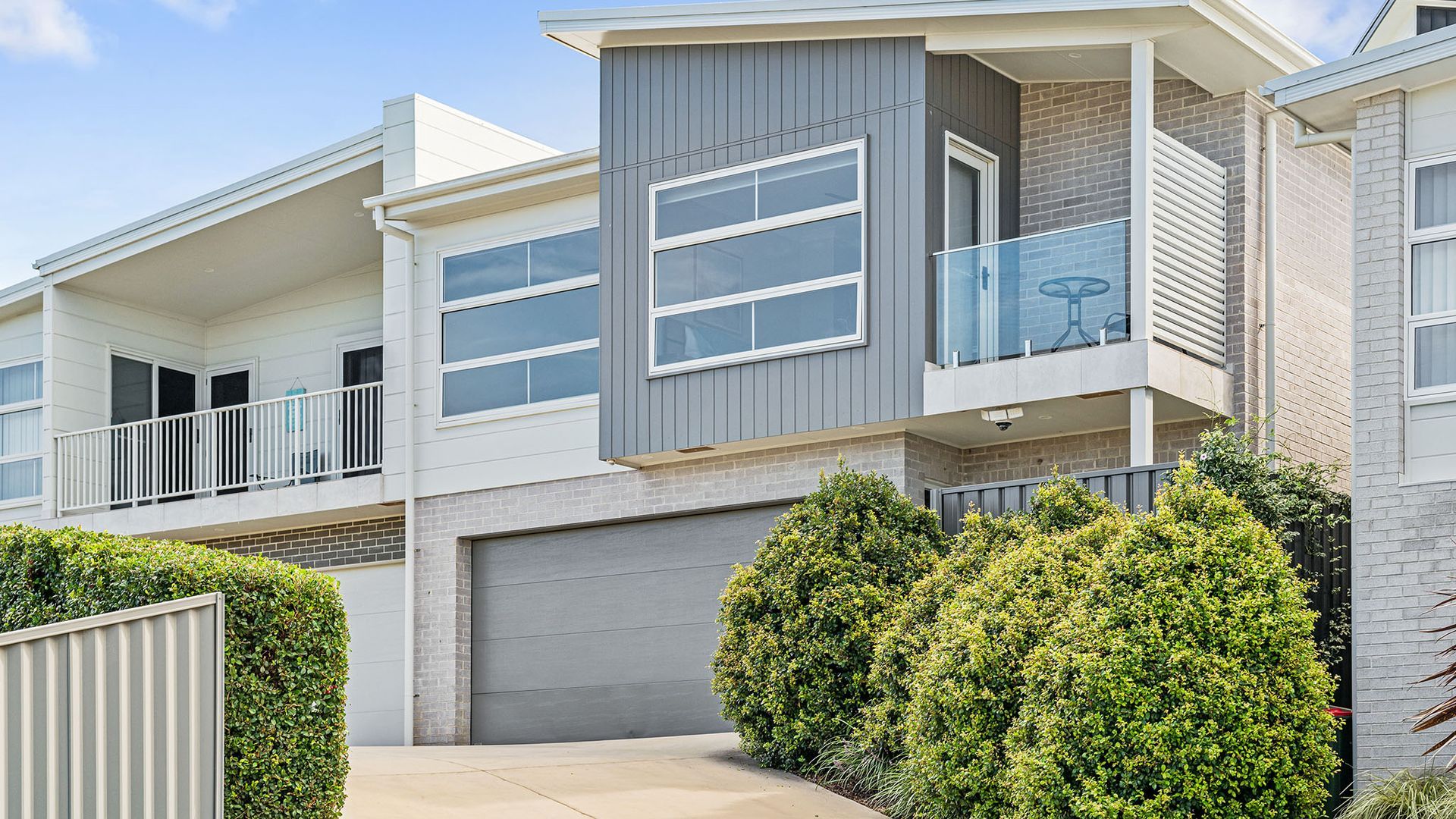A modern two-story residential building with a garage, balconies, and a well-maintained hedge.