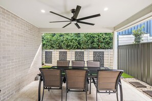 Un portico coperto con un tavolo e sedie in vetro, una ventola a soffitto e un muro in mattoni.