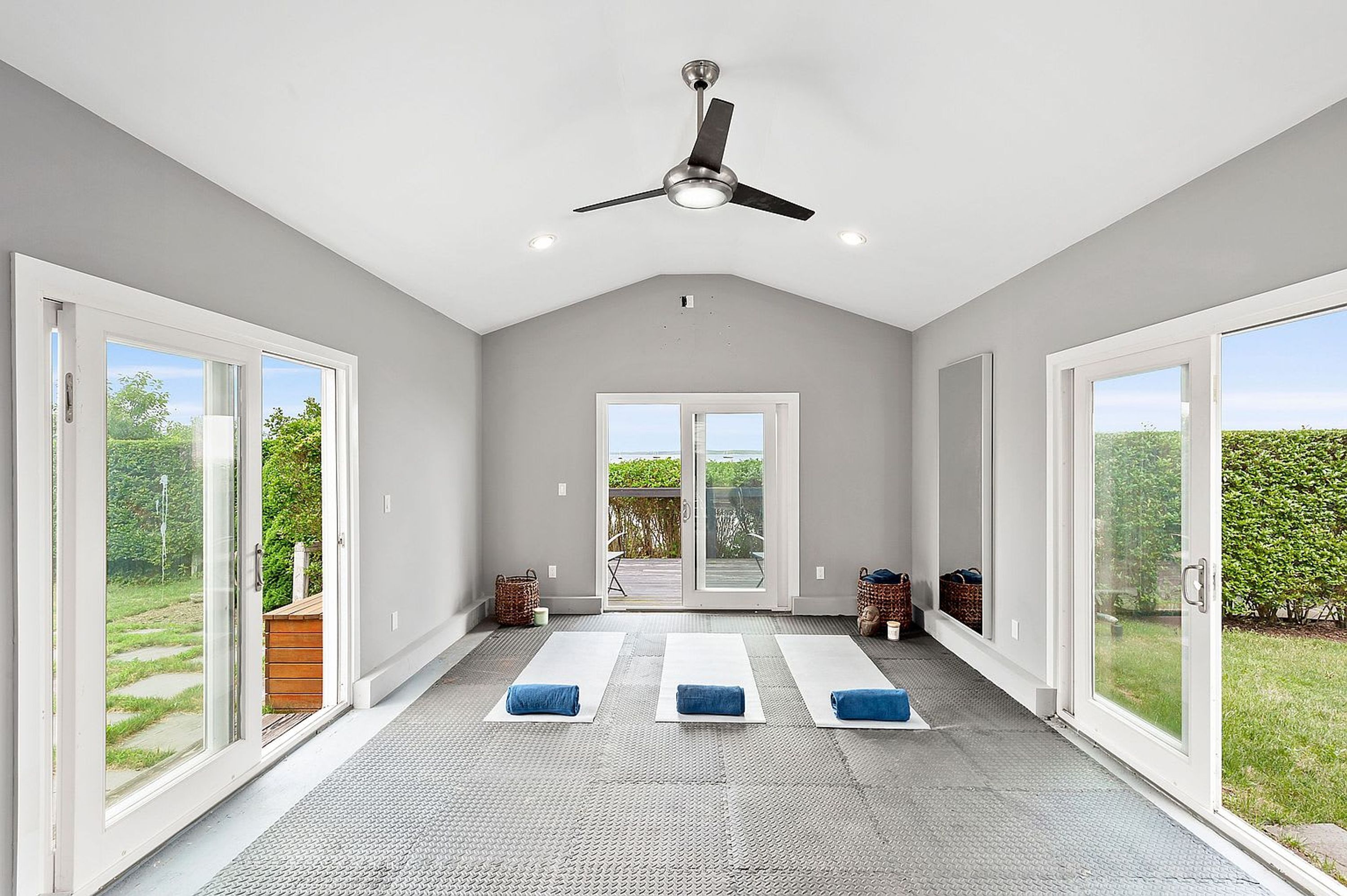 A spacious room with a ceiling fan, large sliding glass doors, and a yoga mat area.