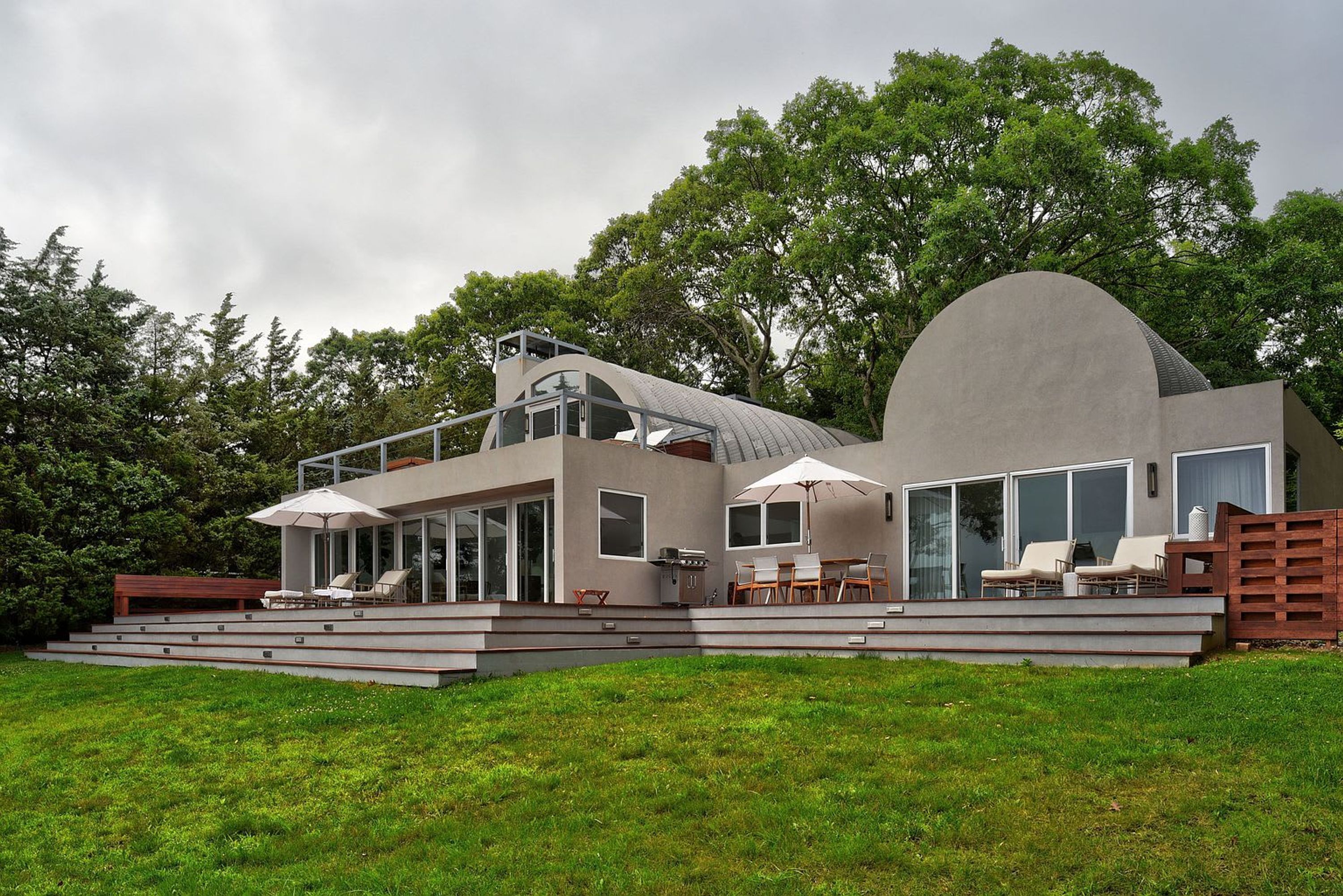 A modern house with a flat roof, large windows, and a patio area with outdoor furniture.