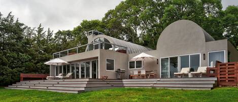 A modern house with a flat roof, large windows, and a patio area with outdoor furniture.
