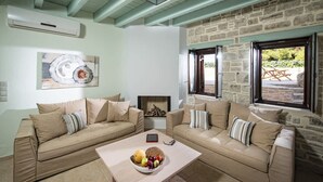 A living room with two beige sofas, a coffee table with fruit, a fireplace, and a stone wall.