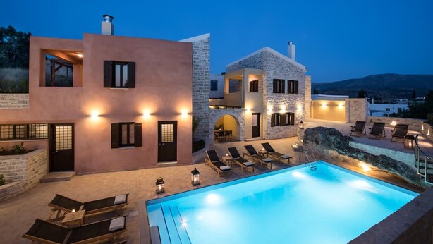 A modern villa with a swimming pool, lounge chairs, and stone architecture.