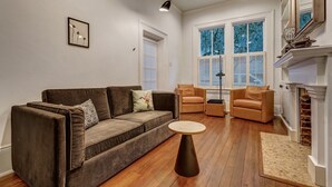 Un salón con un sofá marrón, dos sillones, una mesa redonda de centro y una chimenea.