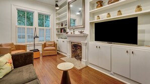 Una sala de estar con chimenea, armarios blancos, un televisor grande y una estantería.