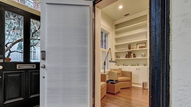 Una habitación con una puerta blanca, un sofá color beige y suelo de madera.