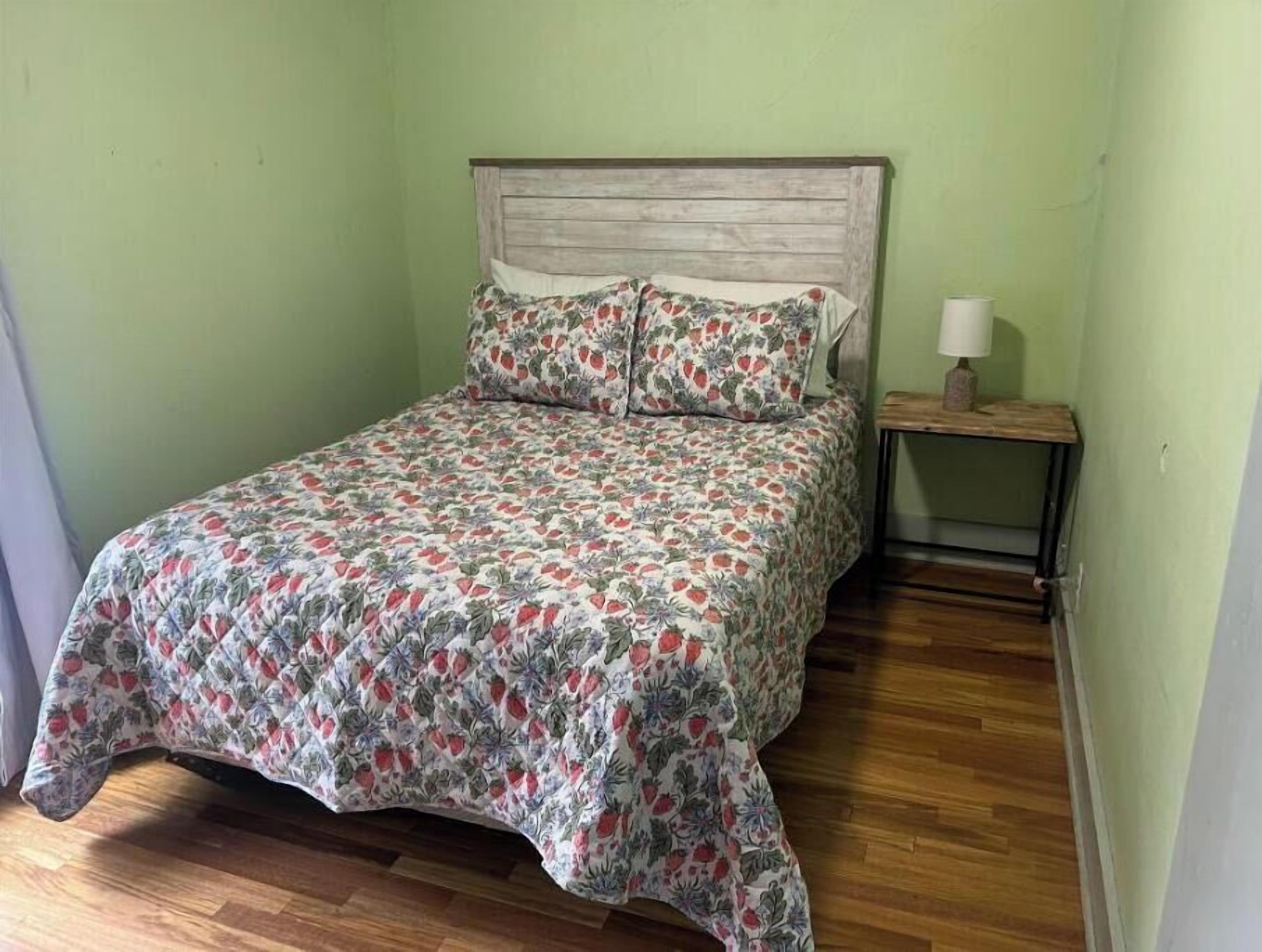 Una cama individual con cubrecama floral, cabecera de madera y mesita de noche con lámpara.