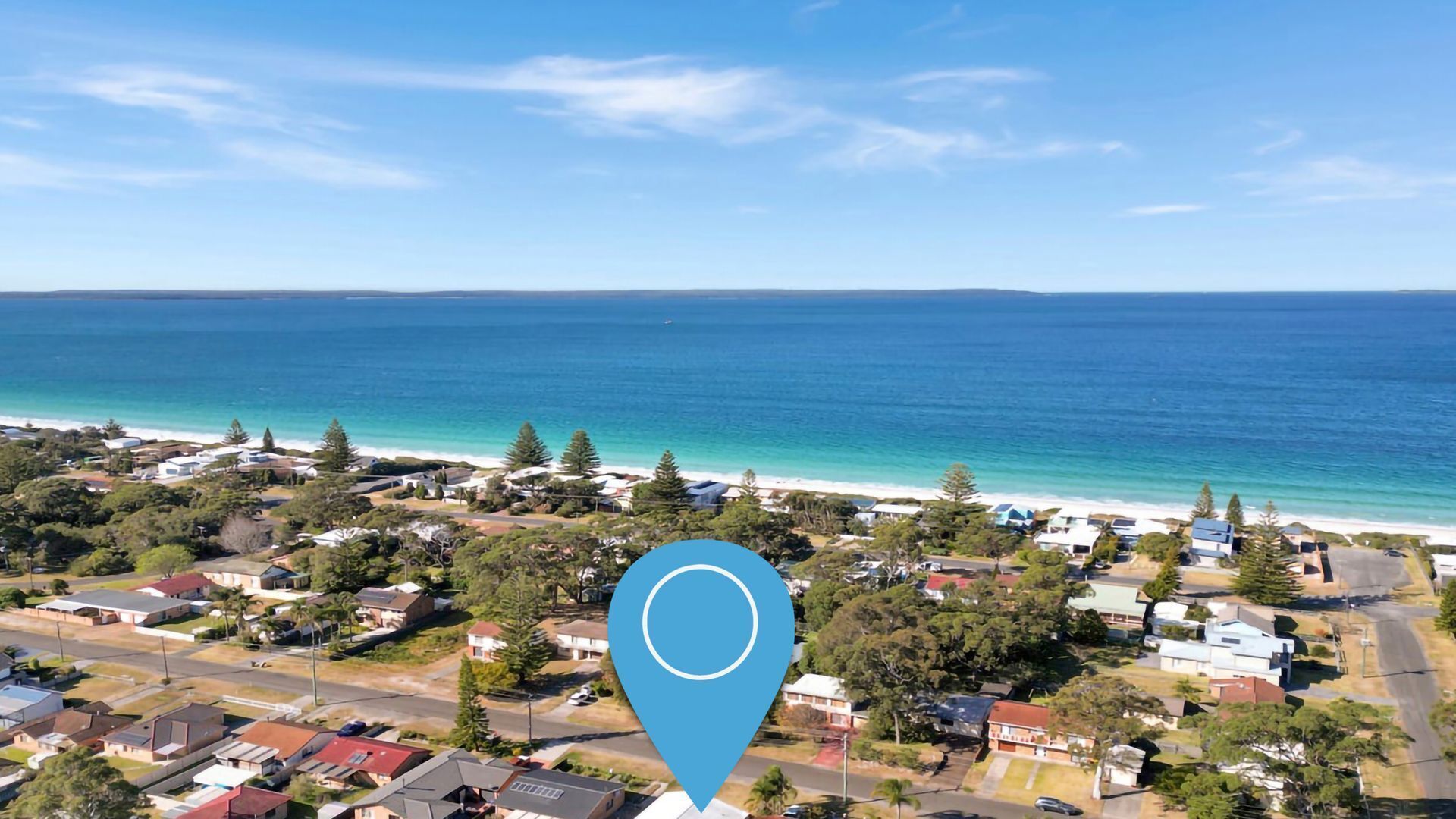 An aerial view of a coastal residential area with houses, roads, and a beach.