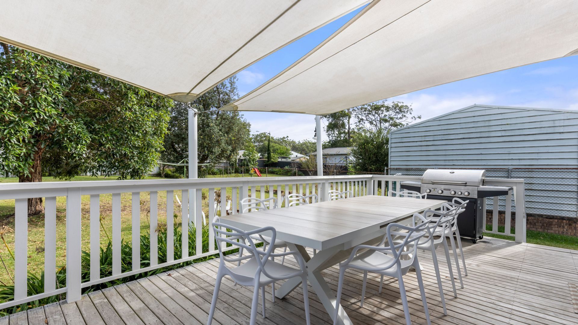 Une terrasse extérieure avec une table et des chaises, un barbecue et une clôture blanche.