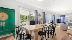 A spacious living area with a wooden dining table, black chairs, a green cabinet, and a TV.