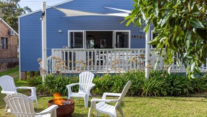 A blue house with a white porch, outdoor seating, and a fire pit.