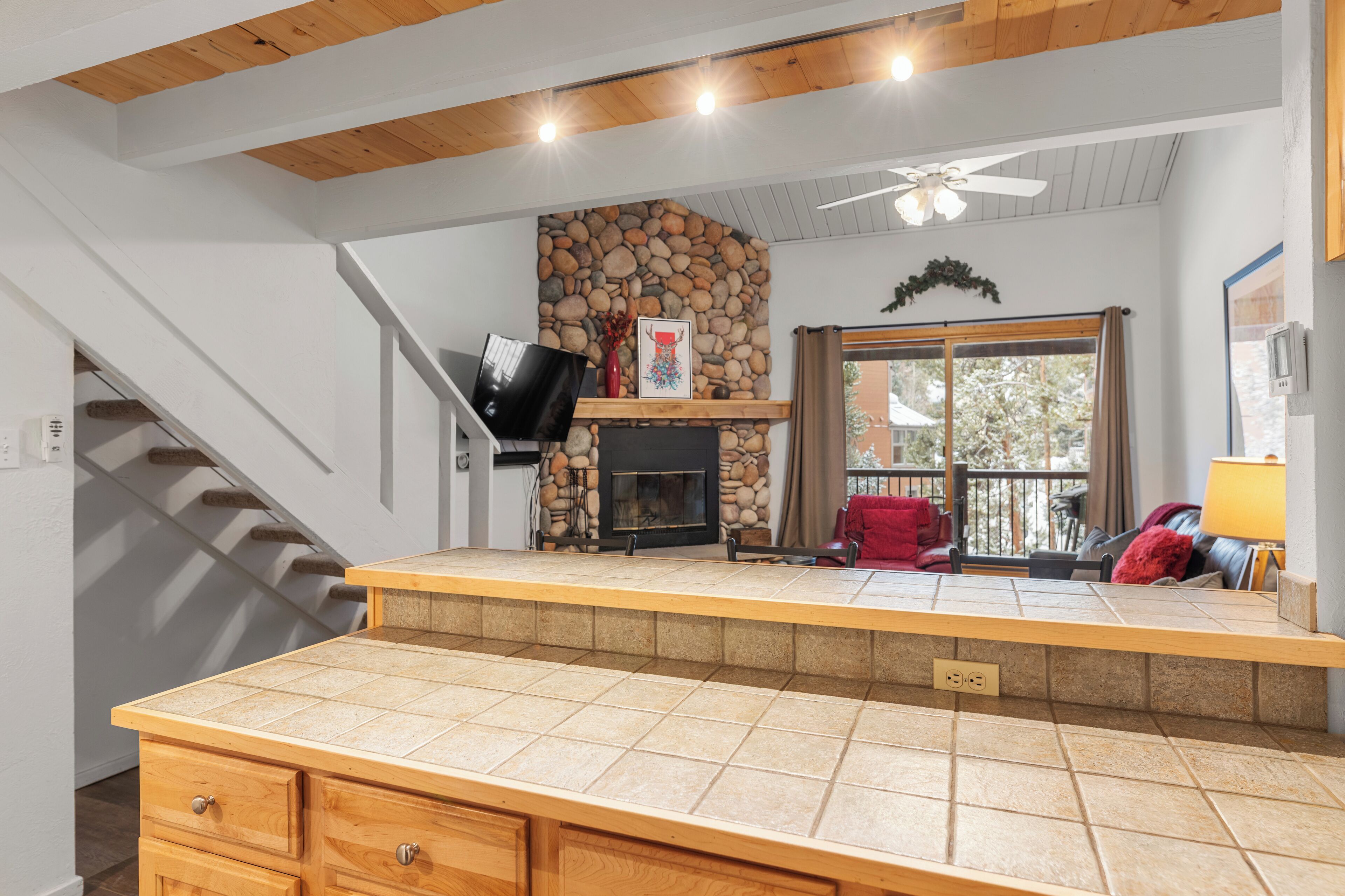A kitchen with a stone fireplace, wooden cabinets, and a tiled countertop.