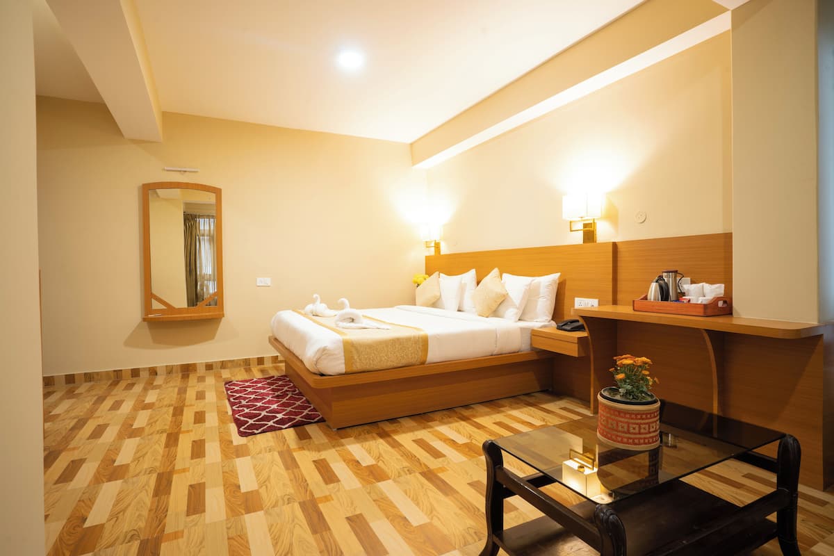 Ein Hotelzimmer mit einem hölzernen Bett, einem Nachttisch mit Lampe, einem kleinen Tisch mit Blumenvase und einem Spiegel an der Wand.