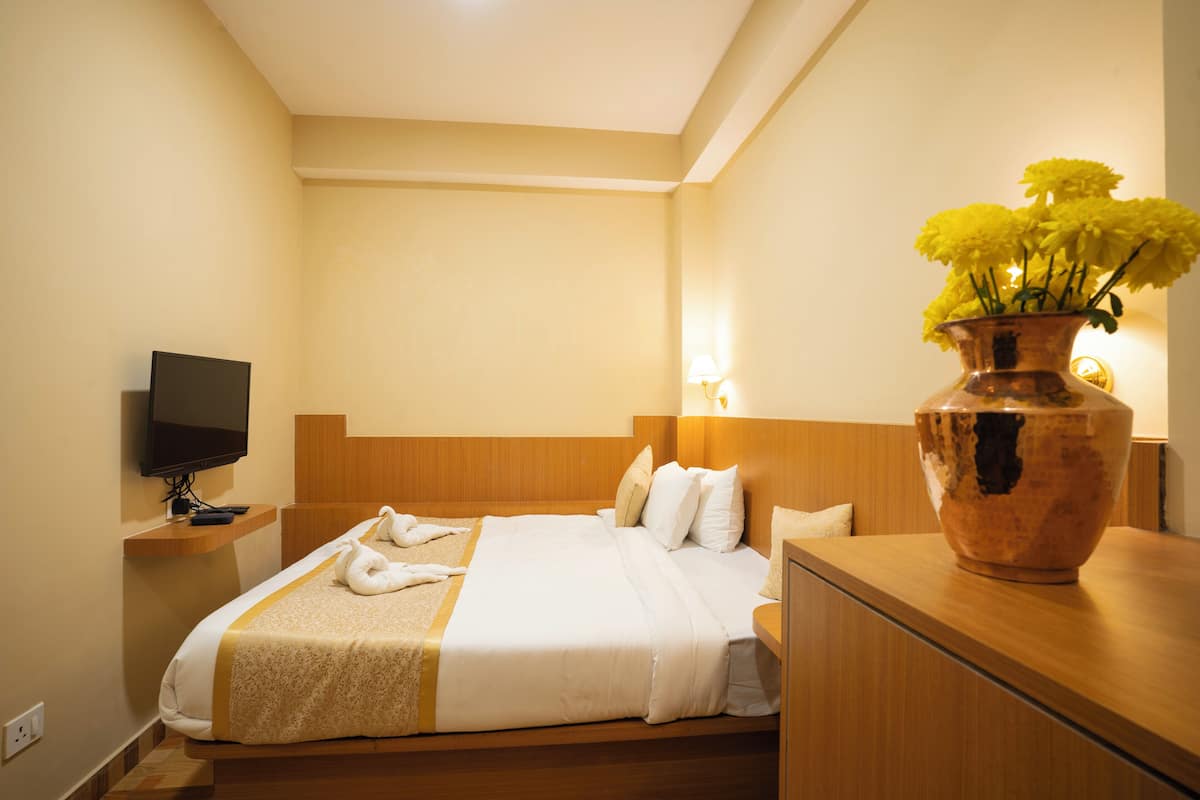 Ein Hotelzimmer mit einem Bett, einem Fernseher, einer Vase mit gelben Blumen und einem Holzkopfteil.