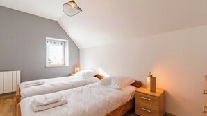 Een slaapkamer met twee bedden, een houten nachtkastje, een nachttafel met een lamp en een raam met uitzicht.