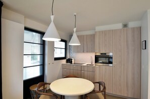 A modern kitchen with a round dining table, two pendant lights, and wooden cabinets. - Amazing Apartment in De Haan Near Beach (De Haan)