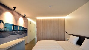 A modern hotel room with a large bed, a wooden wardrobe, and a wall-mounted desk with a beach-themed mural. - Amazing Apartment in De Haan Near Beach (De Haan)