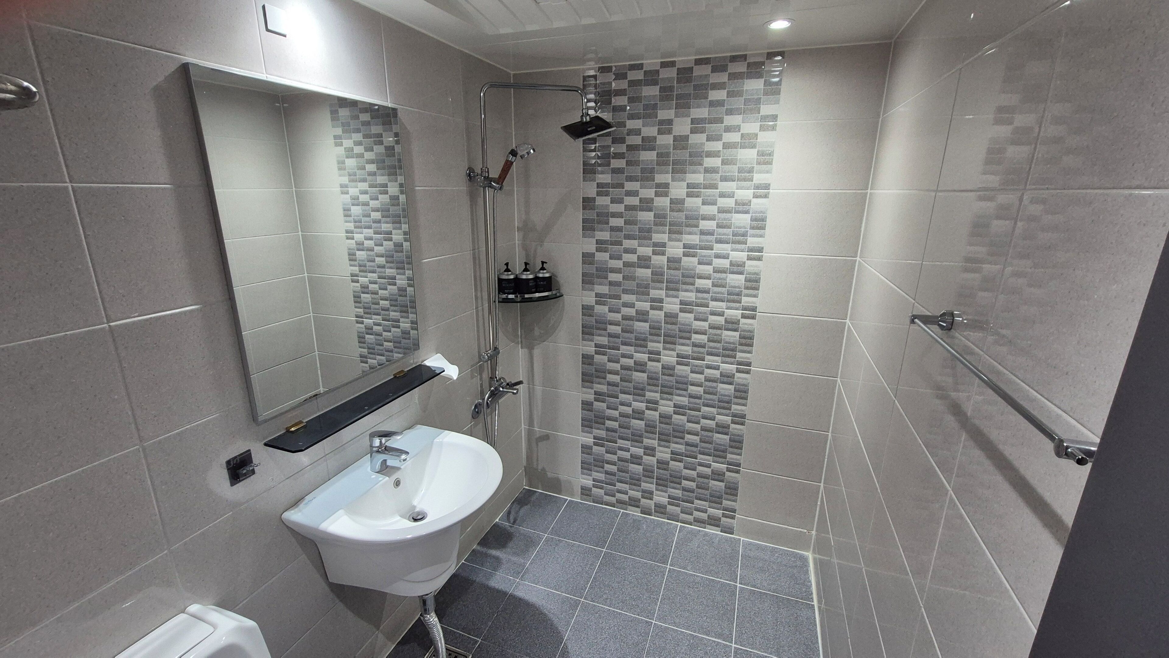 Un baño moderno con un lavamanos blanco, un espejo, ducha con puerta de vidrio y paredes de azulejos.