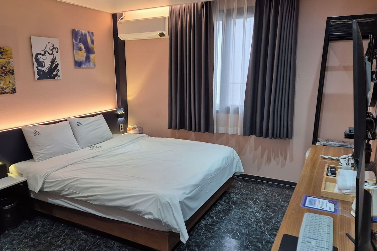 A hotel room with a bed, bedside tables, a desk with a computer, and artwork on the wall.