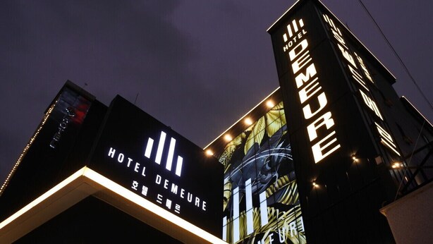 Un hôtel doté d’une enseigne lumineuse, comprenant les inscriptions « HÔTEL DEMEURE » et « HÔTEL DE MEURE » en grandes lettres.