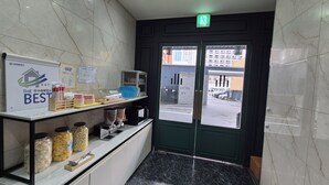 Un hall d’hôtel avec un sol en marbre, un comptoir d’accueil agrémenté de divers objets, et une vue sur la rue à travers une porte vitrée.