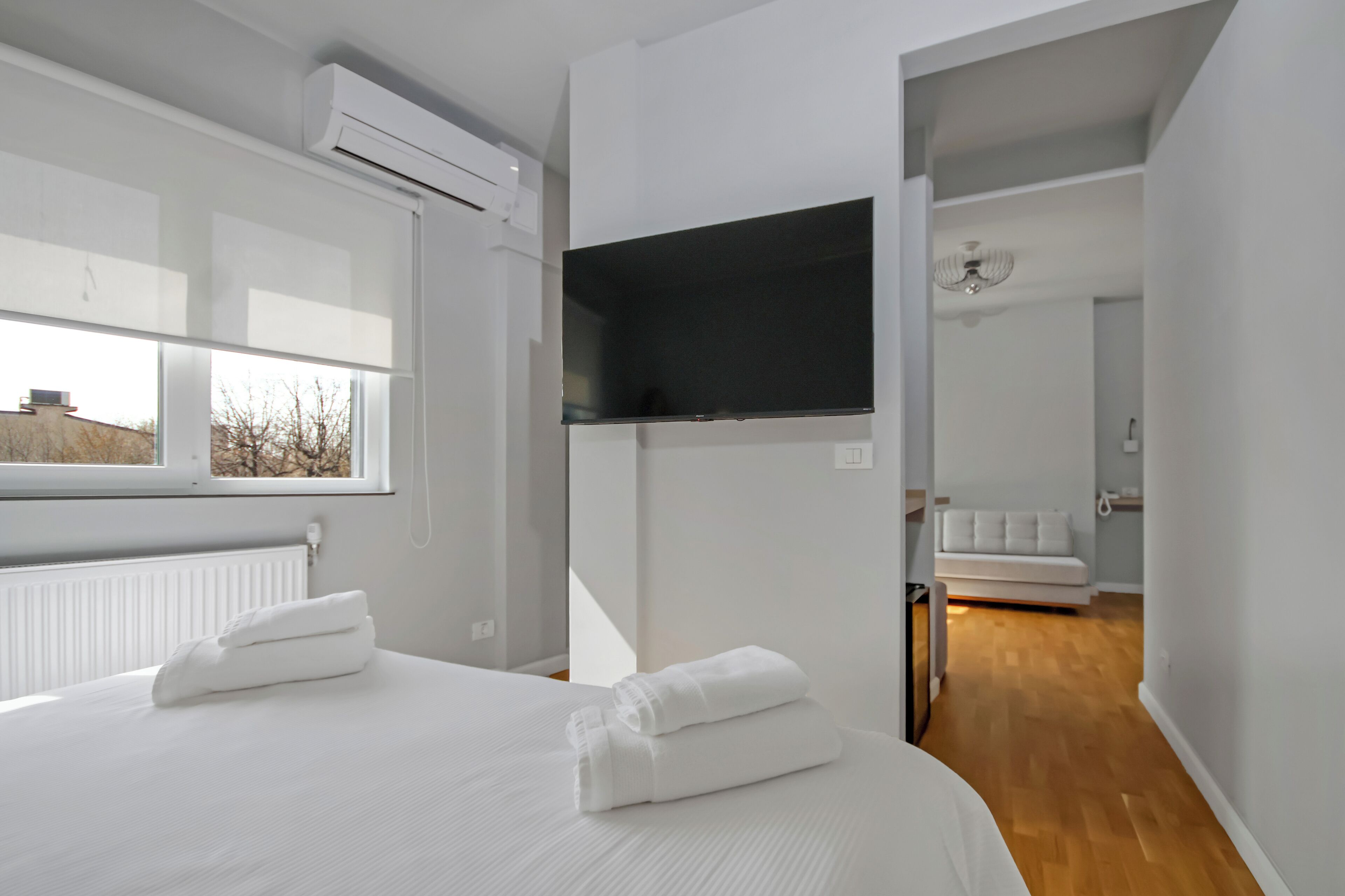 Una habitación de hotel moderna con una cama grande, un televisor de pantalla plana montado en la pared y vistas al exterior a través de una ventana.