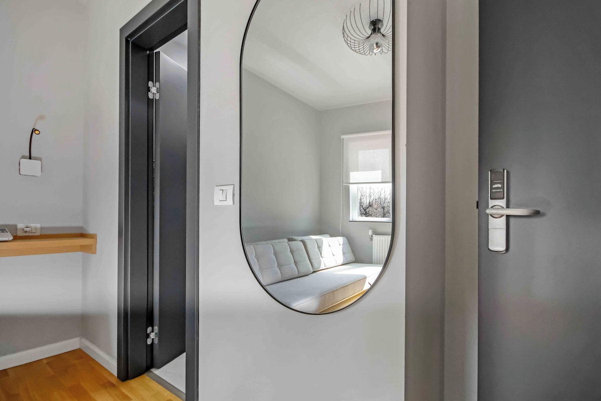 Habitació moderna amb un mirall circular que reflecteix un llit i una finestra.