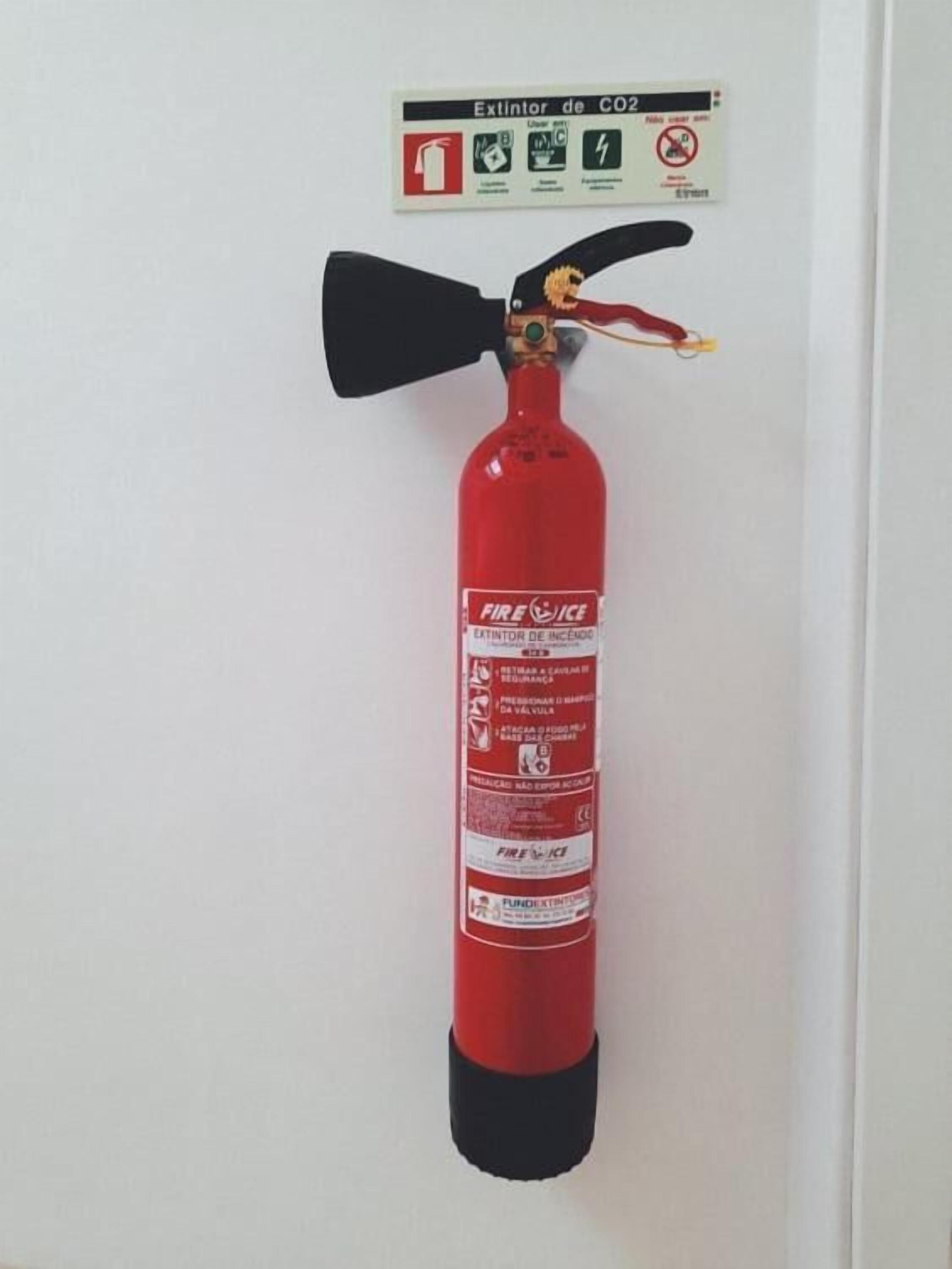 A red fire extinguisher mounted on a white wall, with a sign above it indicating it is a CO2 extinguisher.