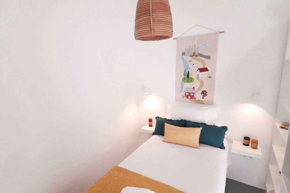 Ein modernes Schlafzimmer mit einem Einzelbett, einer Hängelampe, einem an der Wand befestigten Regal mit Kerzen und einem dekorativen Poster.