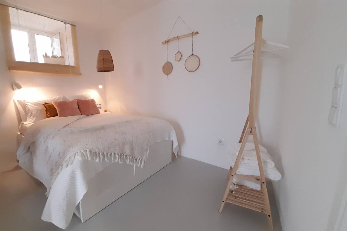 Ein Schlafzimmer mit Bett, einer Hängelampe, einer Holzleiter und einem Wandregal mit runden Gegenständen.