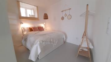 Un dormitorio con cama, lámpara colgante, escalera de madera y un estante con objetos redondos.