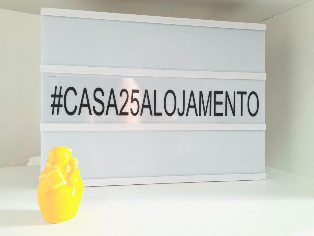 Een bord met de tekst '#CASA25ALOJAMENTO' op een witte achtergrond.