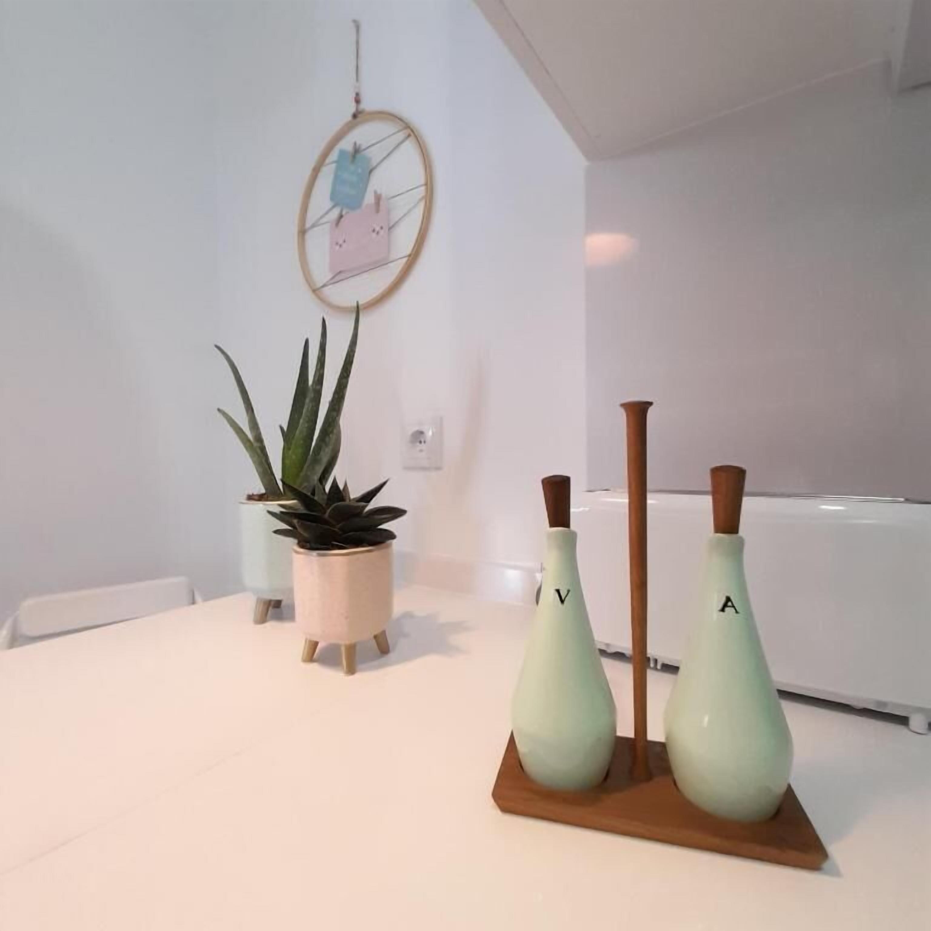 A minimalist room with a white table, a potted plant, two vases, and a wall-mounted circular decoration.