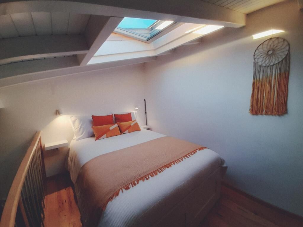 Een slaapkamer met dakraam, een bed met oranje kussens, een nachtkastje en een decoratie aan de muur.