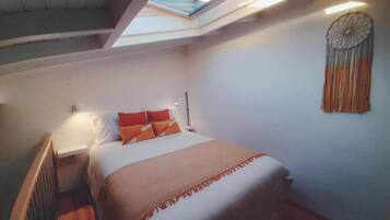 Een slaapkamer met dakraam, een bed met oranje kussens, een nachtkastje en een decoratie aan de muur.