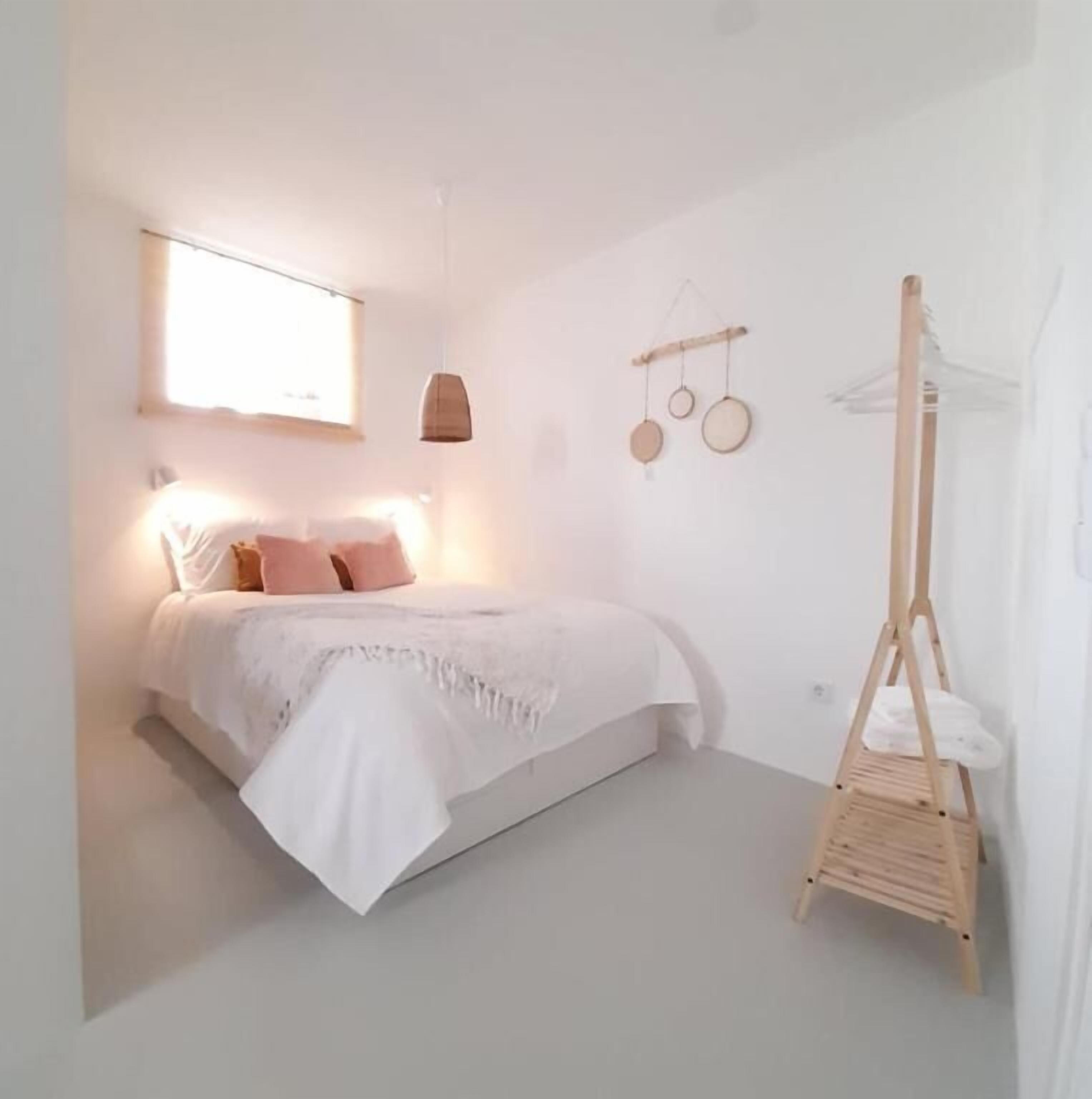 Un dormitorio minimalista con cama, lámpara de noche y una silla colgante de madera.