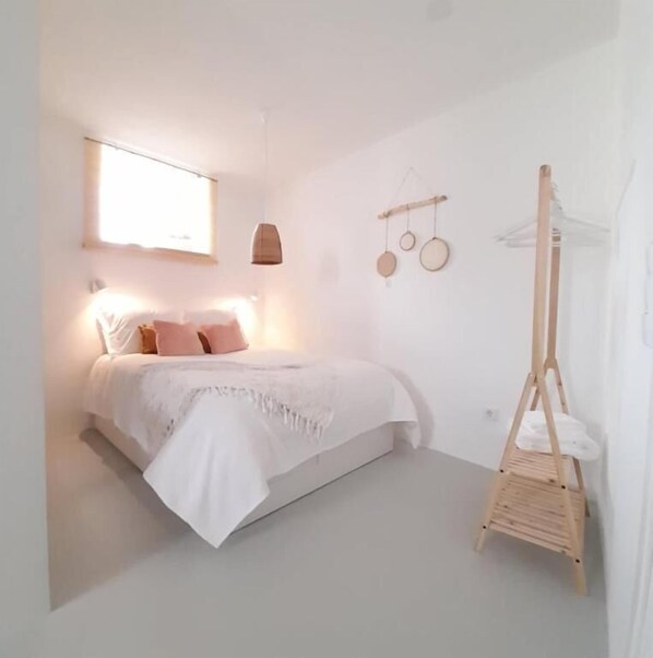 A minimalist bedroom with a bed, bedside lamp, and a wooden hanging chair. - Casa Vinte & Cinco - Alojamento Local (Idanha-a-Nova)