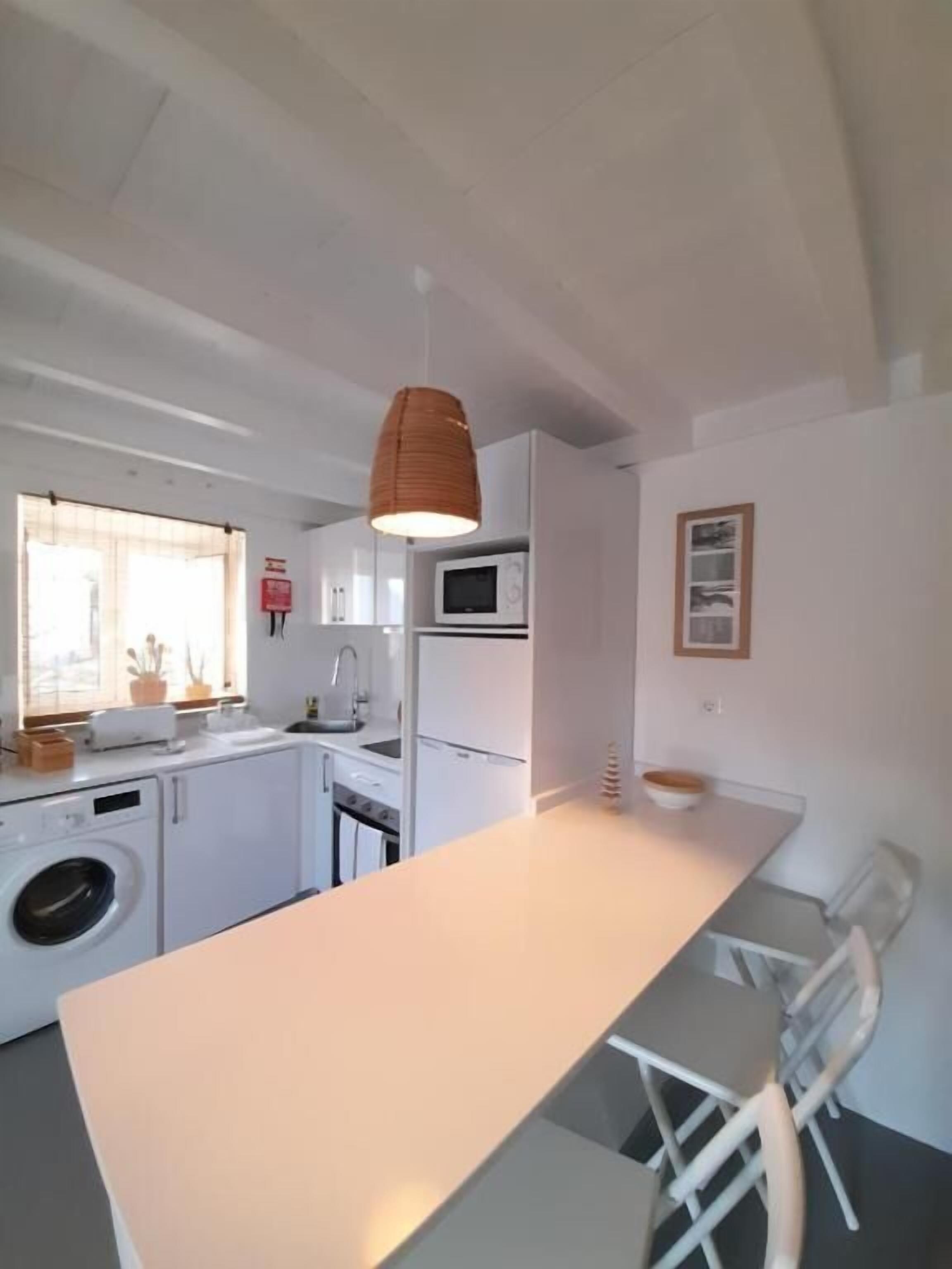 A modern kitchen with a central island, a washing machine, a microwave, and a dining area with chairs.