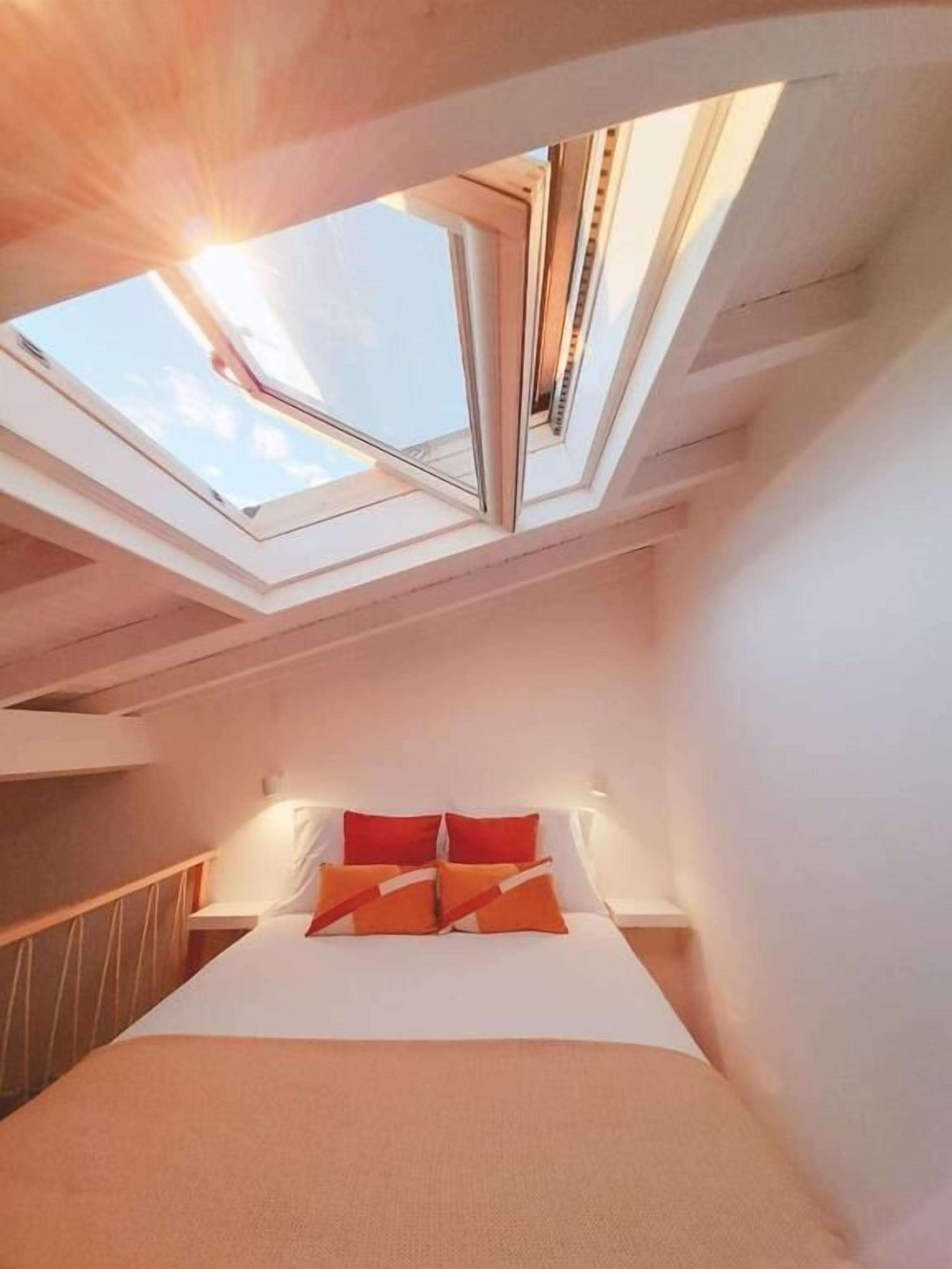 Ein Schlafzimmer mit Dachfenster, einem Bett mit orangefarbener Bettwäsche und einem Holz-Kopfteil.