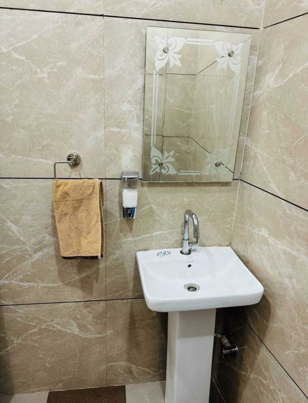A bathroom with a white sink, a towel rack with a towel, a glass mirror with a floral design, and a soap dispenser.