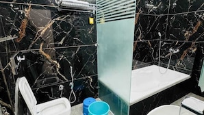 Ein modernes Badezimmer mit schwarzen Marmorwänden, einer Duschkabine aus Glas, einer weißen Toilette, einem Waschbecken und einem Handtrockner.