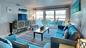 Un salon comprenant un canapé, une table basse, un téléviseur et un balcon aménagé avec du mobilier d’extérieur.