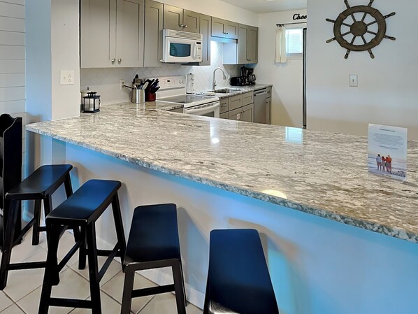 A kitchen with a granite countertop, a microwave, a coffee maker, and a ship's wheel decoration. - 2BD/2BA Sea Oats 309 | Pool/Hot Tub, Private Beach Access, Prime Location (Fort Walton Beach)