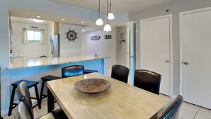 Ein Essbereich mit einem langen Tisch, Stühlen, einer Schüssel, einer Theke mit Spüle und einer Wand mit Steuerrad und Schild.