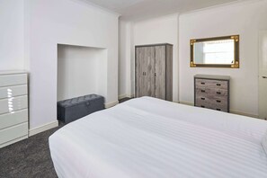 Un dormitorio con cama, armario, cómoda, banco y espejo en la pared.