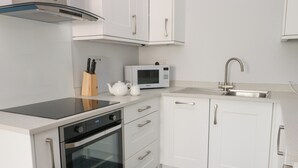 Ett modernt kök med vita skåp, en rostfri köksfläkt, en mikrovågsugn, en diskho och en svart induktionshäll.