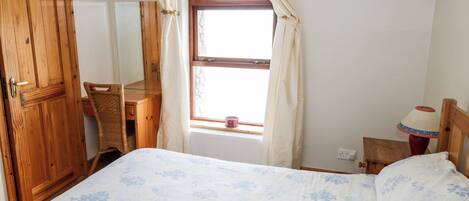 A bedroom with a bed, wooden wardrobe, desk, and a window with curtains.