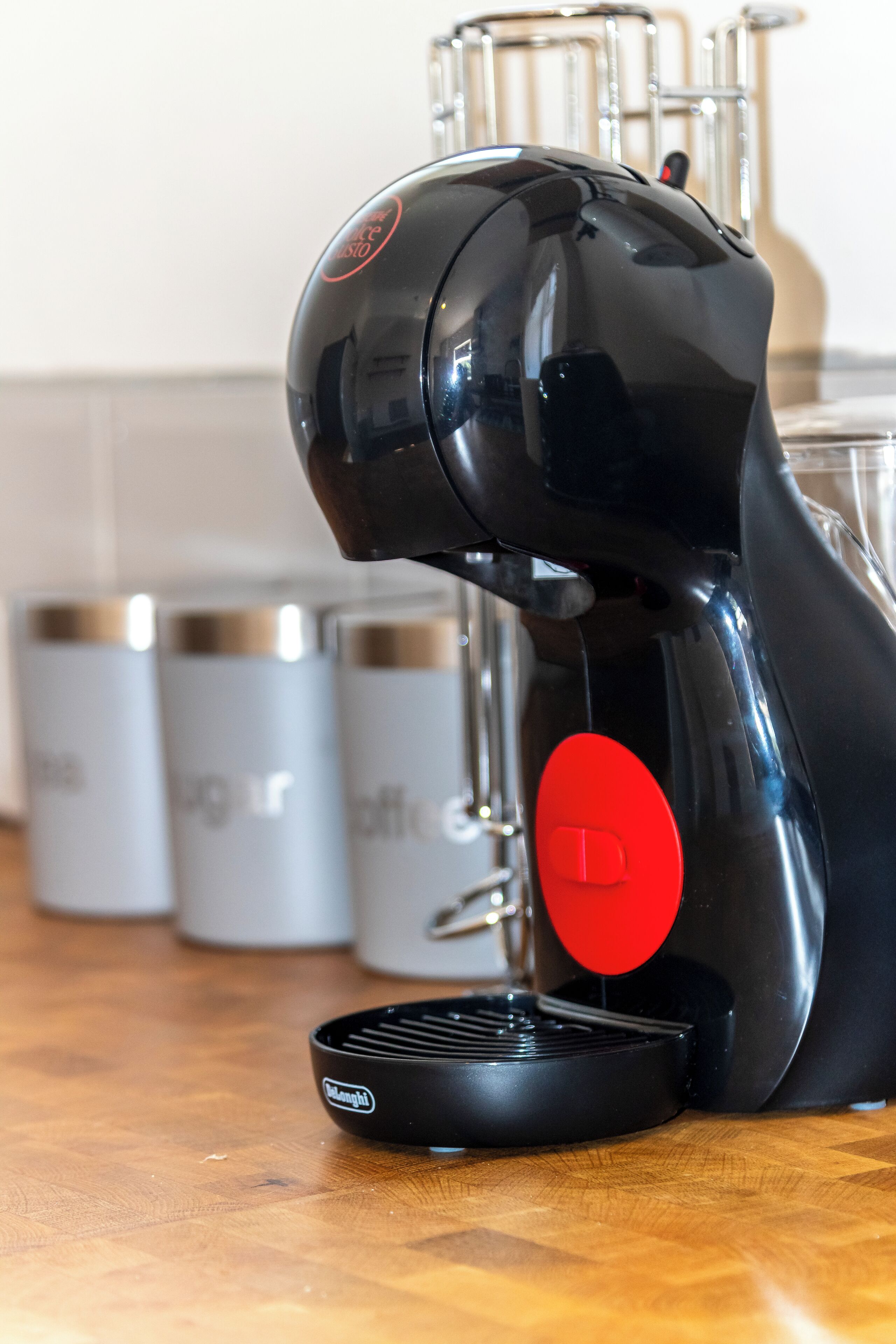 A coffee machine with a red button, a black base, and a transparent container in the background.